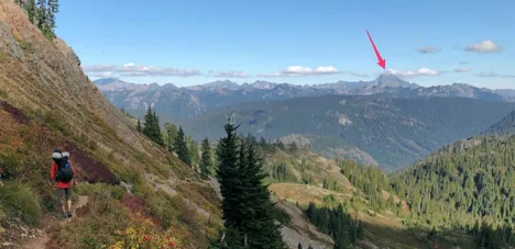 A hiker on a trail looking at a distant peak